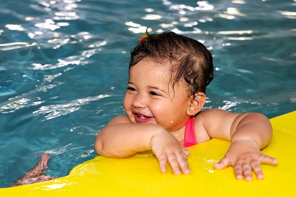 A happy little girl swimming in pool with yellow floatie.