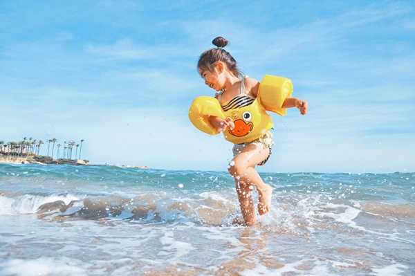 Little girl gleefully playing in ocean near a sandy shoreline. 