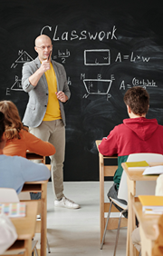 A male teacher stands in front of large blackboard teaching class.