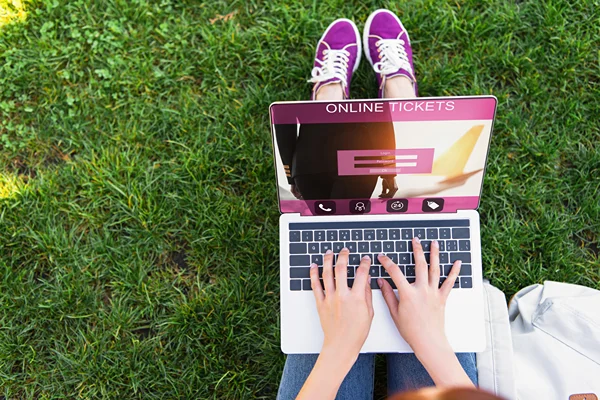 Someone sitting on grass and buying tickets on a laptop.