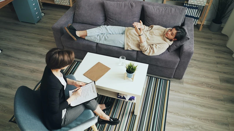 School counselor sitting in chair as student is talking while laying on sofa.