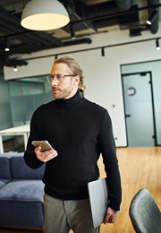 Well dressed man enters tech office holding smartphone with one hand and laptop with the other.