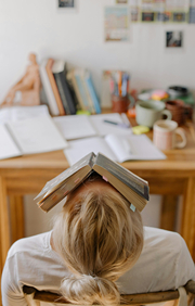 Student at desk laying back on chair with book over her face.