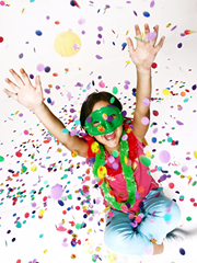 Smiling tween girl with party mask throwing glitter.