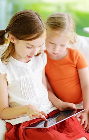 Little girl with younger sister engaging on a tablet.