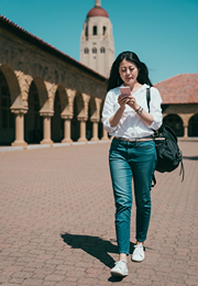 Young female tourist is looking at her phone while walking by old building.