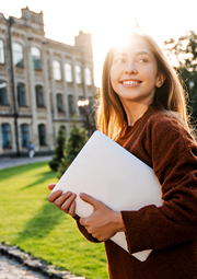 Young woman looking back and smiling as she walks towards old college building.