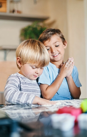 Two boys playing with flour on the kitchen counter.