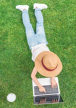 View from top of girl laying on grass browsing on laptop.