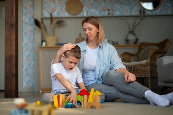 Autistic boy sitting on the floor with his mom playing with toys.