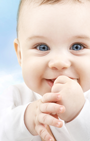 Closeup of a smiling baby with blue sky and cloud behind.