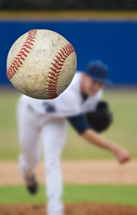 Close up of baseball coming in as pitcher completes throw in the background.