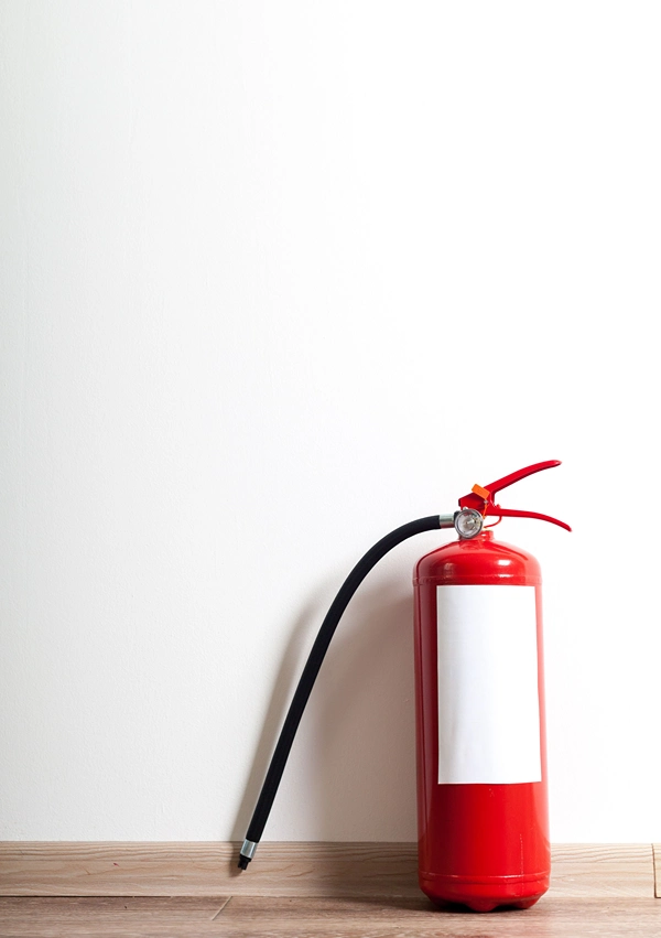 A fire extinguisher on the floor in front of white wall.