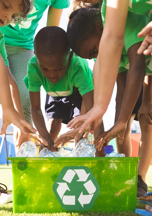 Group of kids putting plastic bottles in recycling bin.