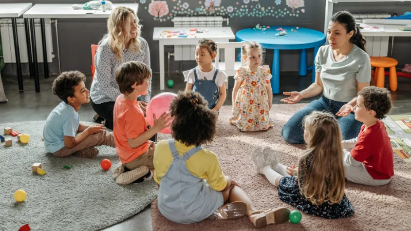 A group of kids in daycare setting learning from two caregivers.