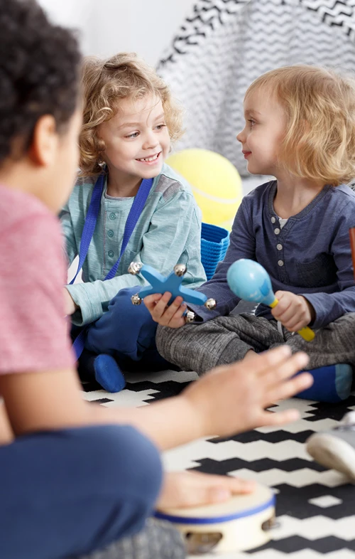 Daycare kids playing instruments on floor.