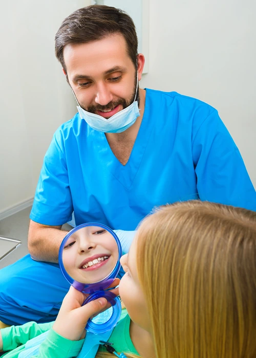 Girl smiles into a hand held mirror at the dentist.