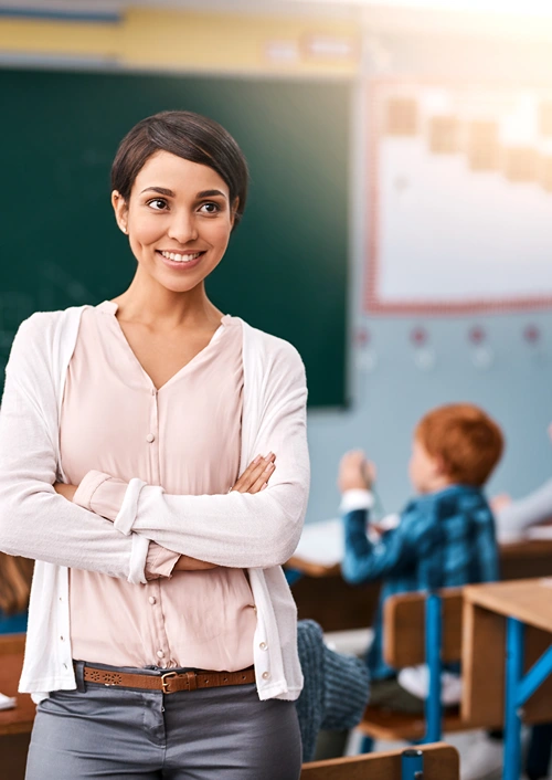 Female teacher smiling in her classroom with students in the background.