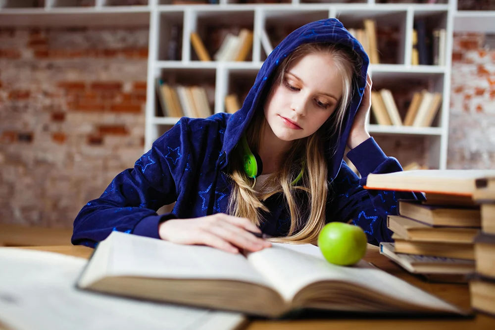 Teen girl in blue jacket reading book.