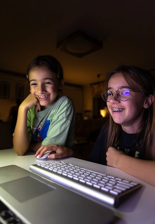 Tween girl surfs the web as her friend watches. Both are smiling and having fun.