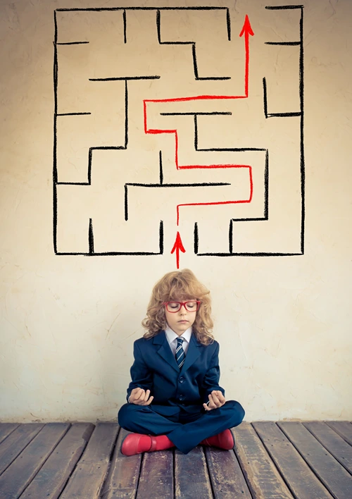 Child mediating under a maze puzzle on the wall above.