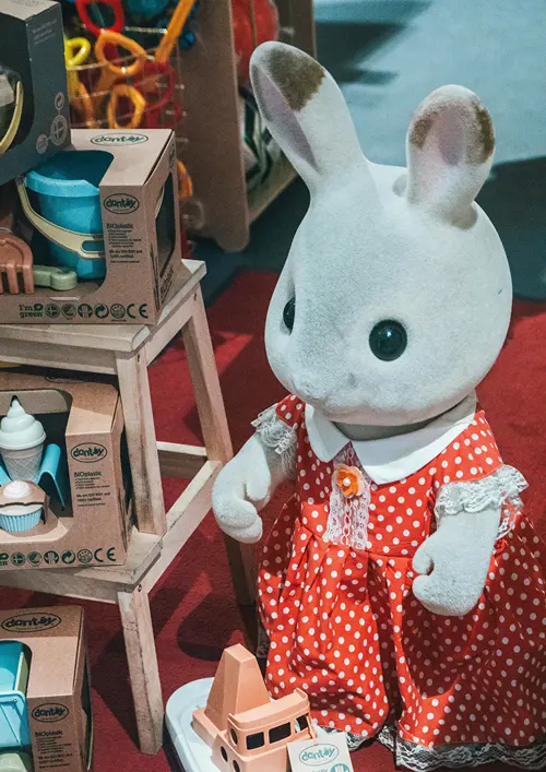 A bunny in a dress beside other toys in a toy store.