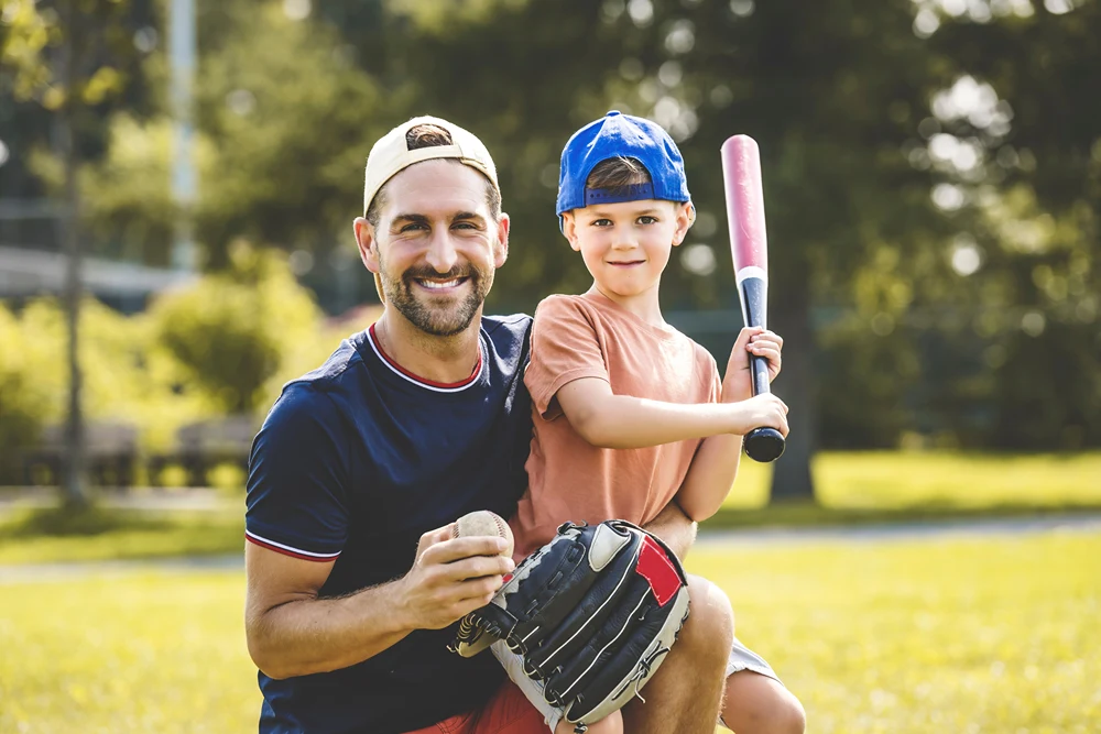 Dad holds up son as the boy holds a baseball bat.