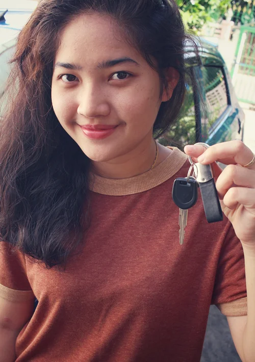 Female teen standing by a car while holding up the keys and smiling.