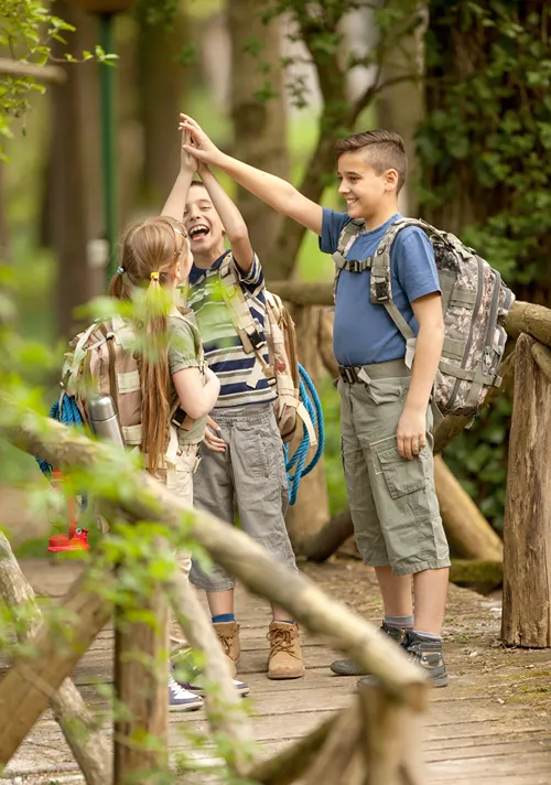 Kids with backpacks crossing wooden footbridge.