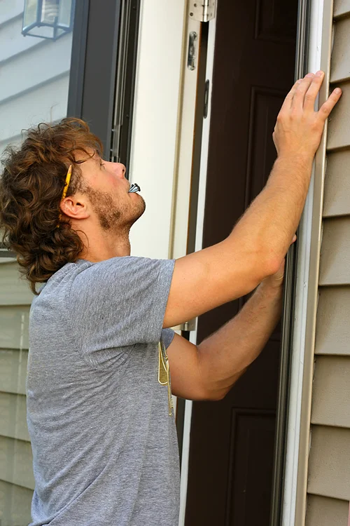 Man outside fixing door trim after a storm damage.