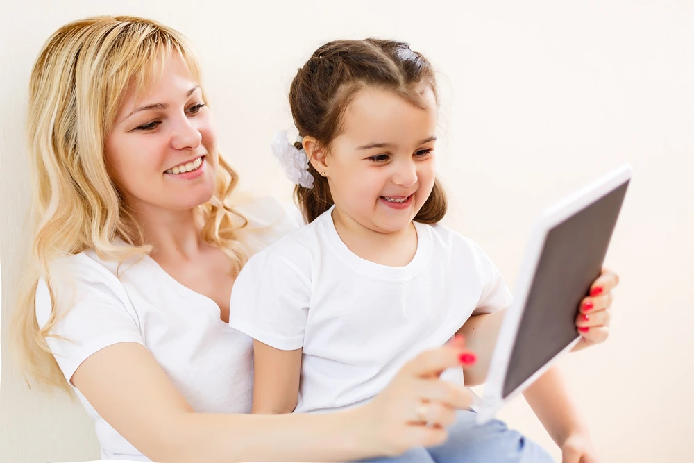 Little girl sits on mom's lap as they look at a tablet together.