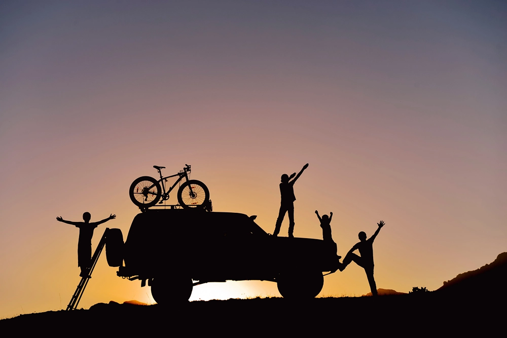 Silhouette of an SUV with bike on top as family celebrates their off-road adventure.