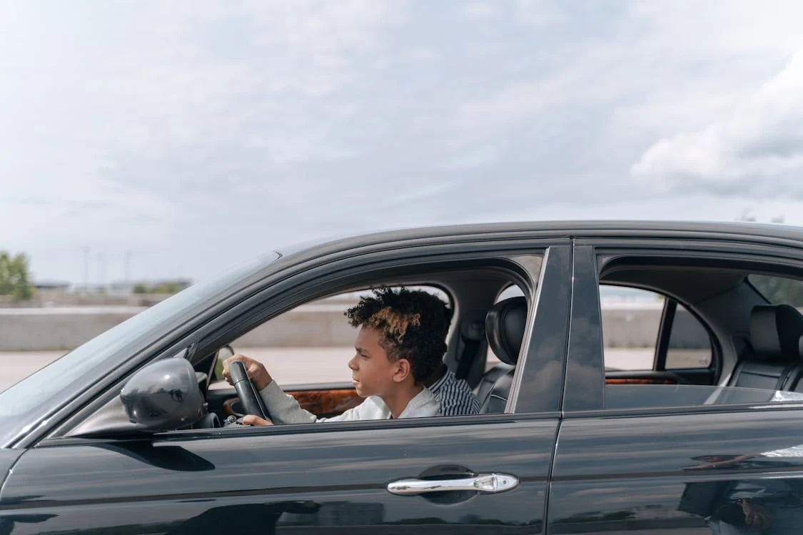 A male teen is focused as he drives a car along on the highway.