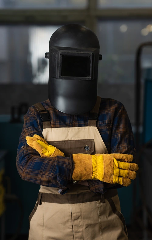 Fully covered female welder donning helmet, gloves and overalls.