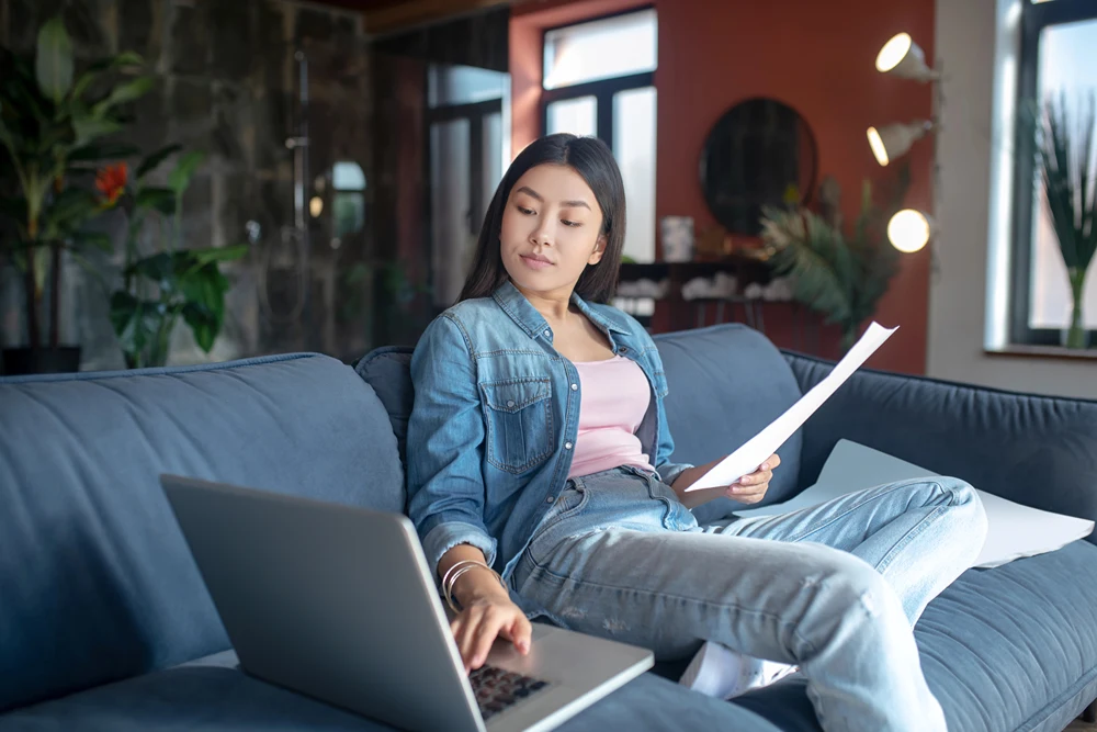 A young woman sits on a couch taking an online class on her laptop.