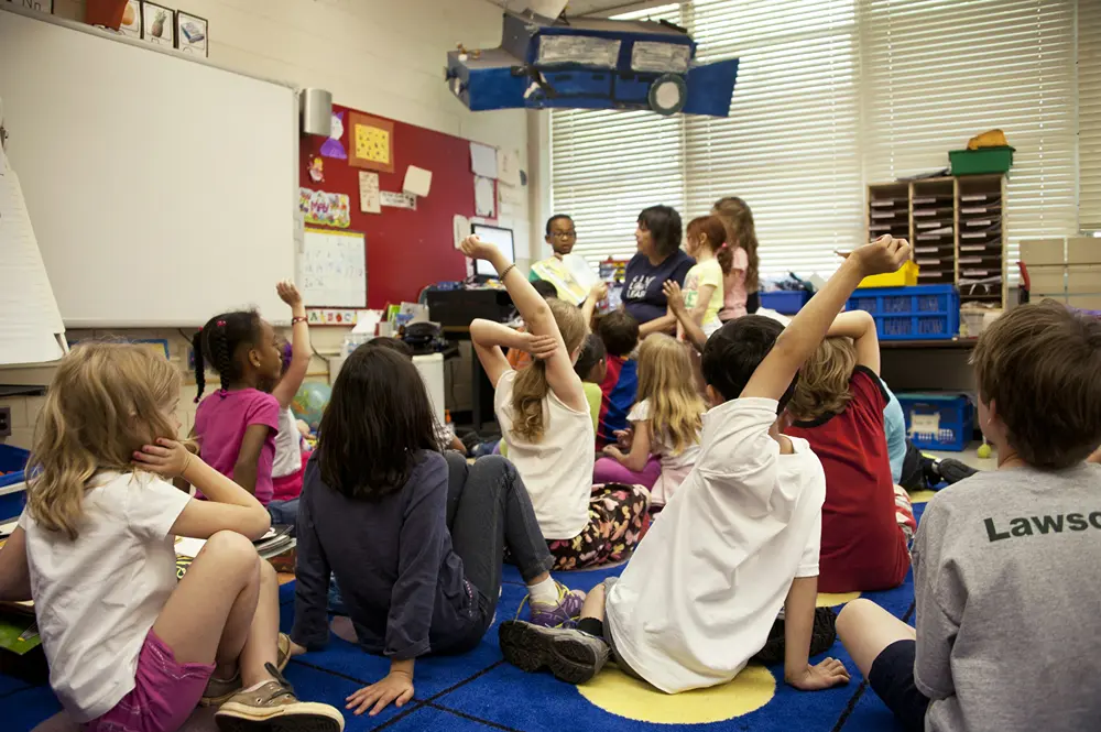 Large group of children on carpet in classroom listening to their teacher.