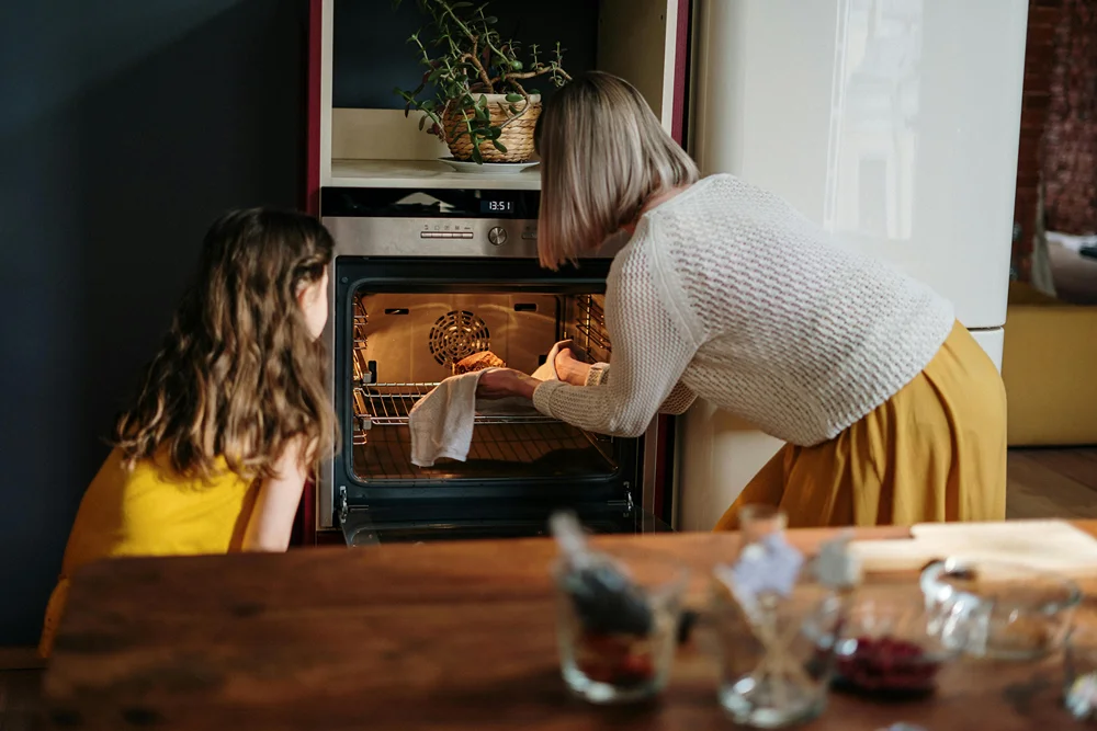 A little girl and woman removing hot bread from the oven.