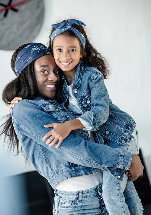 Happy African American mother holds her tween daughter, who is also smiling.