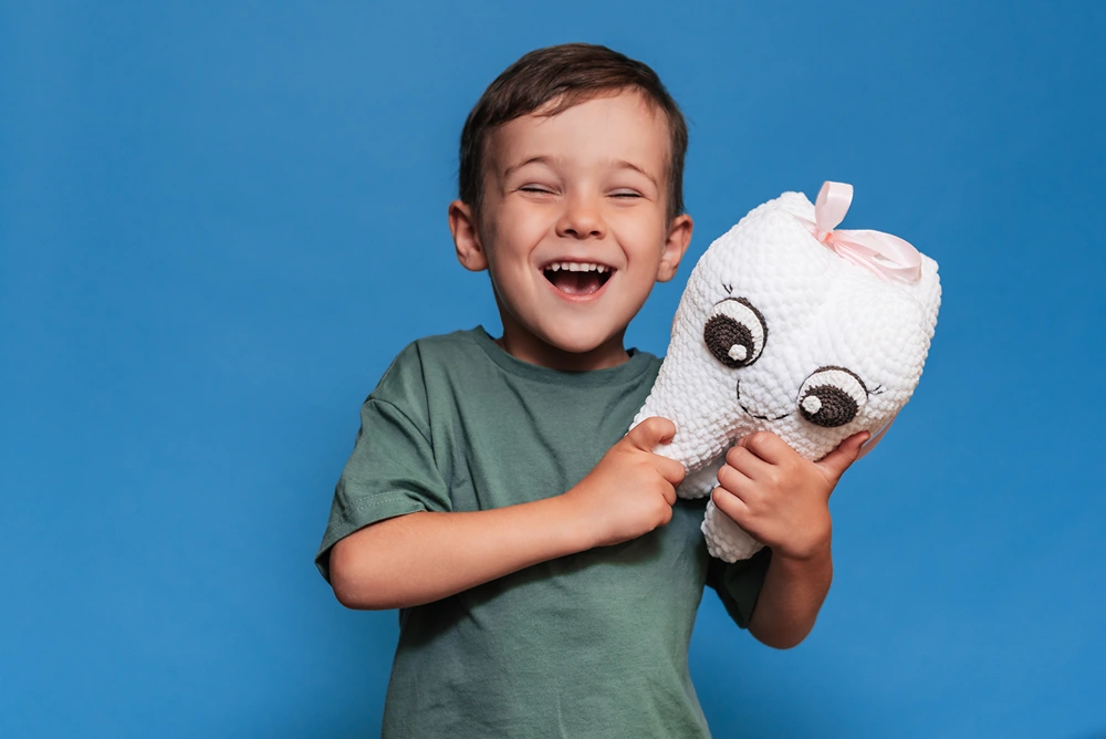 A boy is holding a stuffed tooth and smiling.