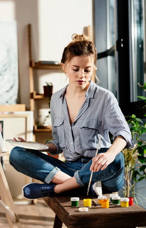 A contemplative female artist painting in her studio.