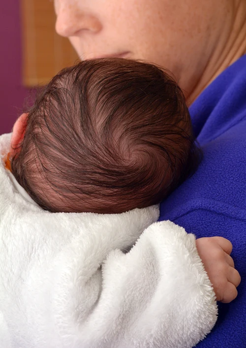 Baby in a sleep sack held closely by mother.