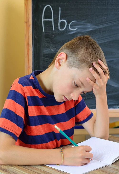 Boy with hand on his forward looking stressed as he works at his classroom desk.