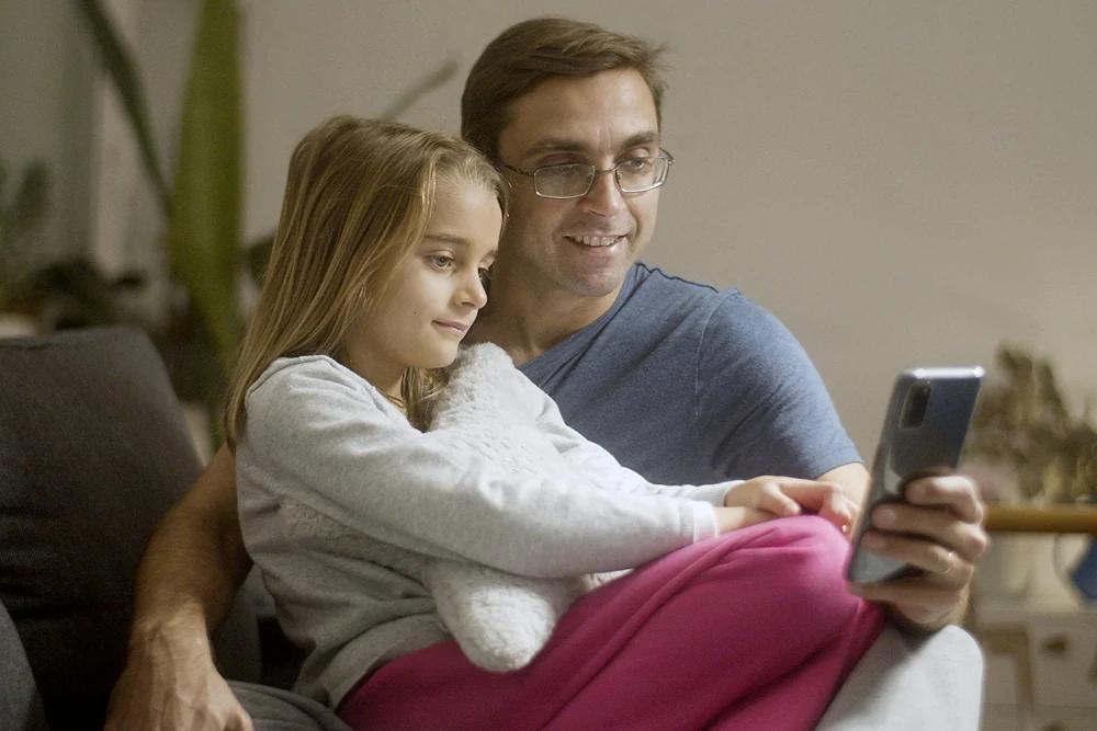 Father and daughter looking at a smartphone screen together.