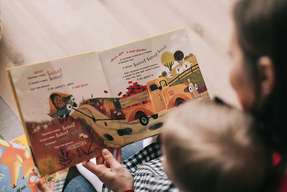 Boy sits on woman's lap as she reads him a picture story book