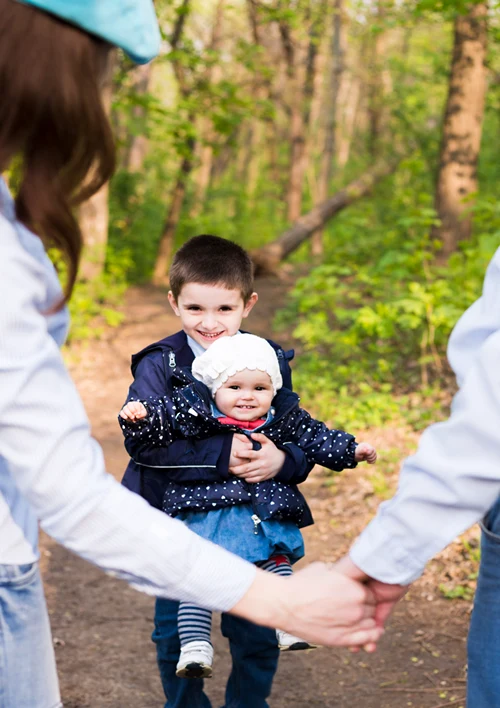 Boy holding baby as he walks outside with this parents.