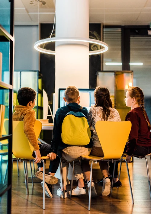 Kids in chairs around a computer in school